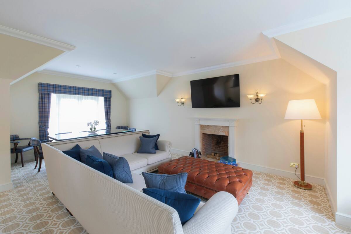 A living room with a sofa, ottoman, fireplace, flat-screen TV, and a lamp.