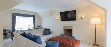 A living room with a sofa, ottoman, fireplace, flat-screen TV, and a lamp.