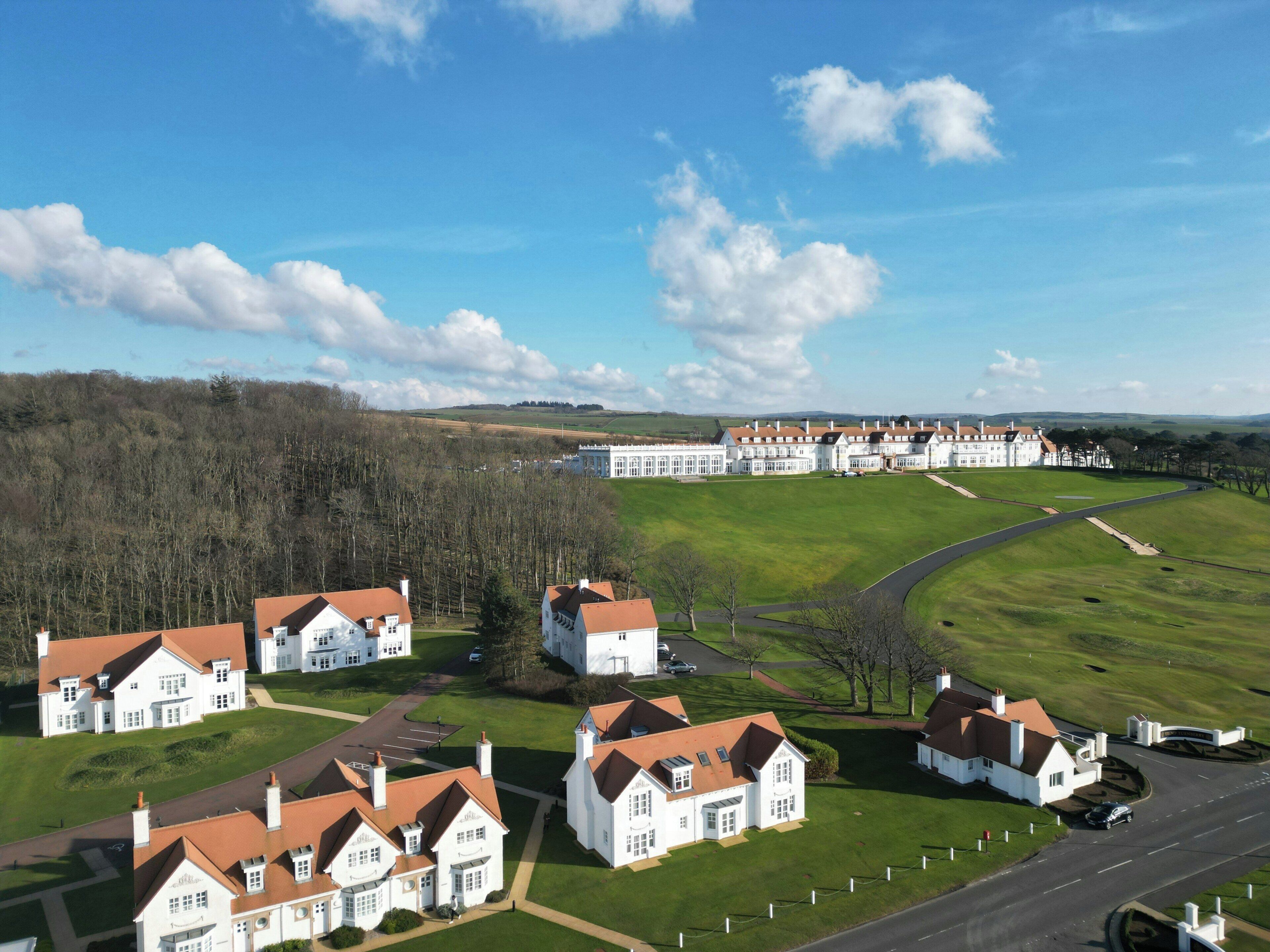 A large estate with multiple white buildings, a well-maintained lawn, and a road leading to the property.