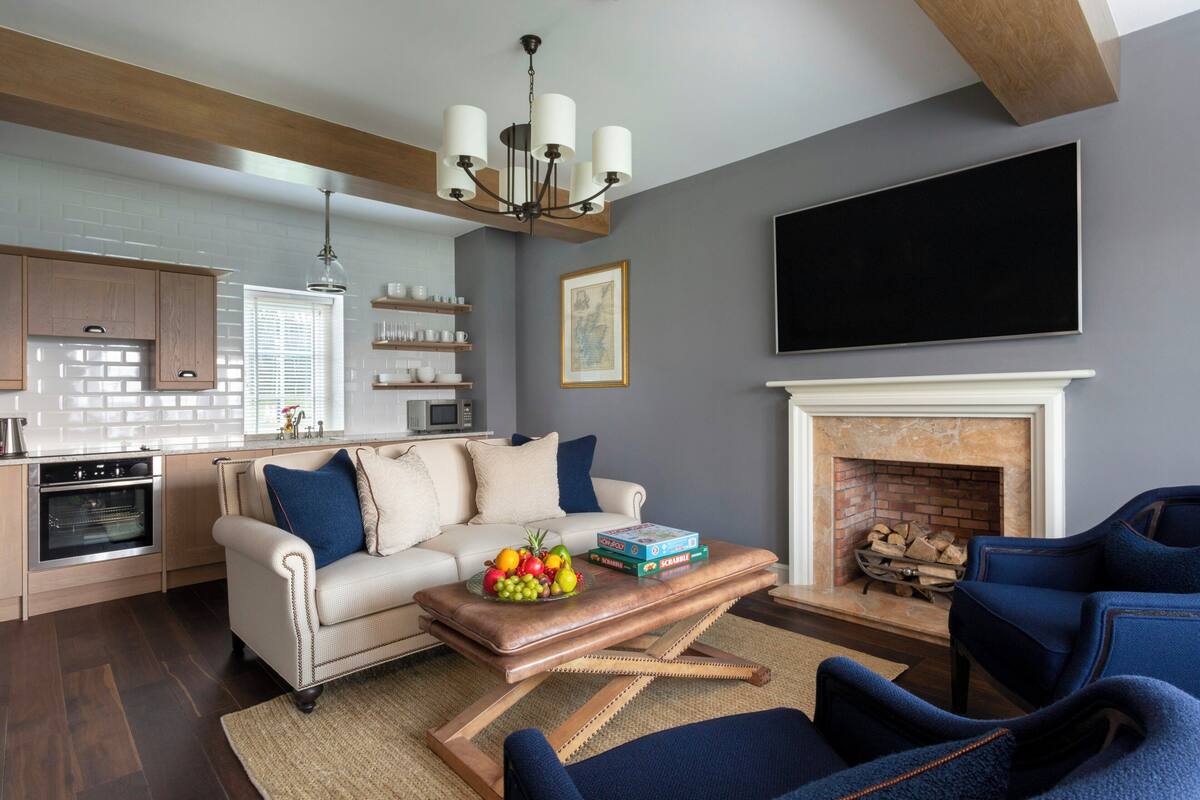 A living room with a sofa, coffee table, and chairs, a fireplace, and a kitchen area with cabinets and a microwave.