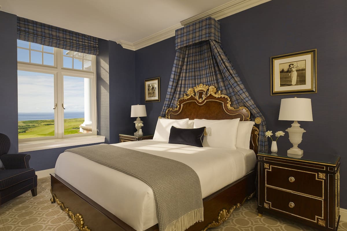 A bedroom with a large bed, a view of the outdoors, a chair, and two nightstands with lamps.