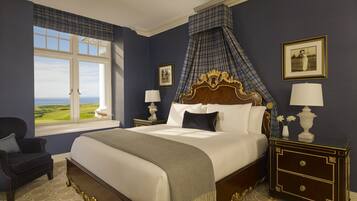 A bedroom with a large bed, a view of the outdoors, a chair, and two nightstands with lamps.