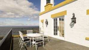 A white building with a lighthouse, a table with chairs, and a view of the sea. - Trump Turnberry (Girvan)