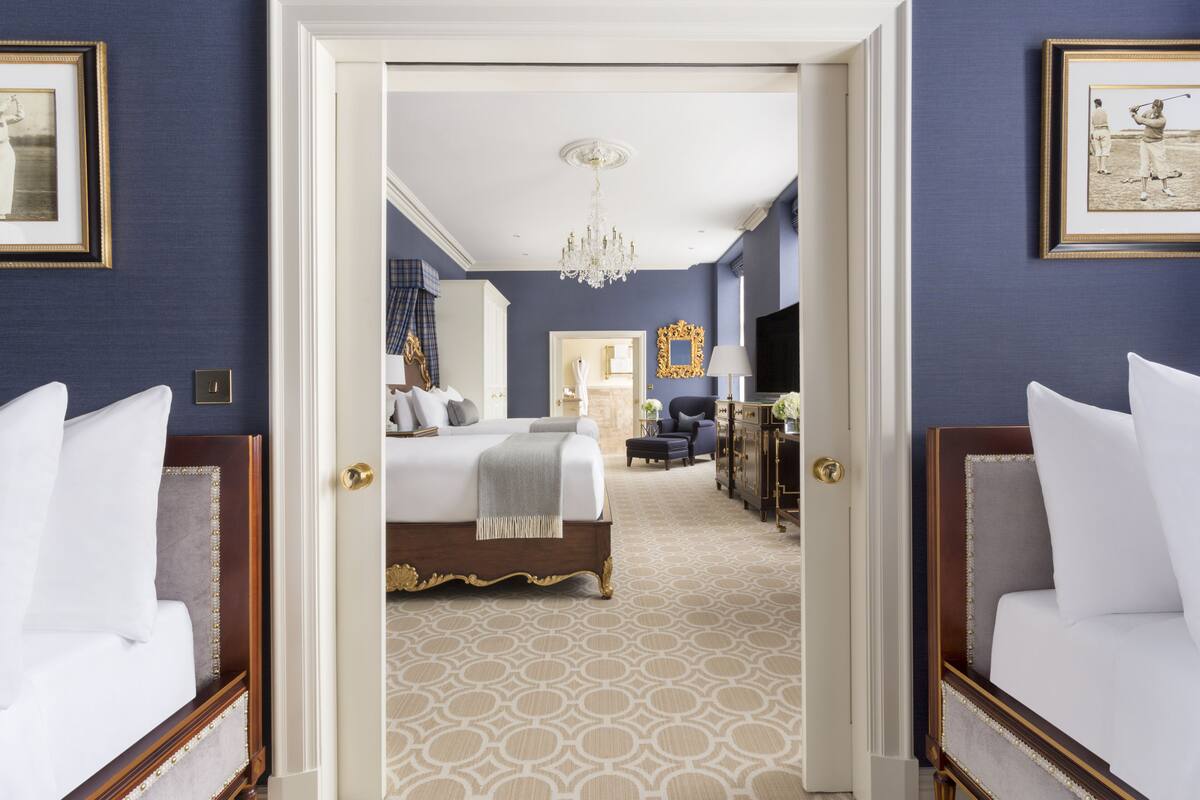 A hotel room with a large bed, a desk, and a chair. There is a chandelier hanging from the ceiling.