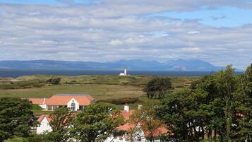 Eine Küstenlandschaft mit einem markanten weißen Gebäude, einem Leuchtturm und fernen Bergen.
