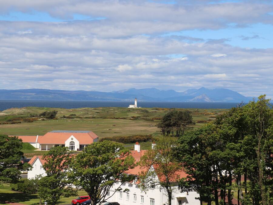 Eine Küstenlandschaft mit einem markanten weißen Gebäude, einem Leuchtturm und fernen Bergen.
