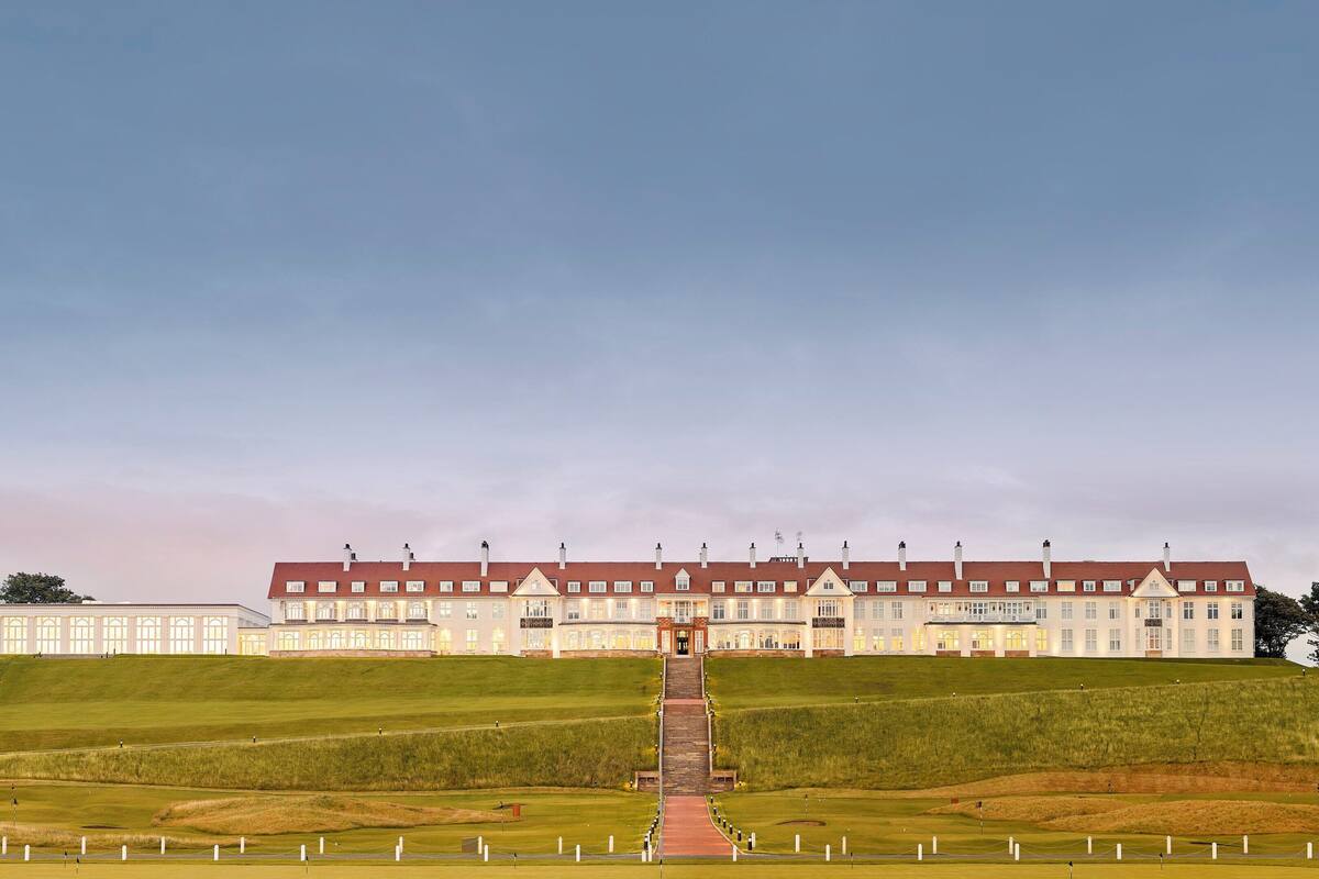A large building with a long driveway leading to the entrance, surrounded by well-maintained grass and white bollards.