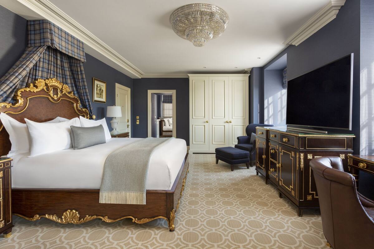 A spacious bedroom with a large bed, a television, a wardrobe, and a chandelier.