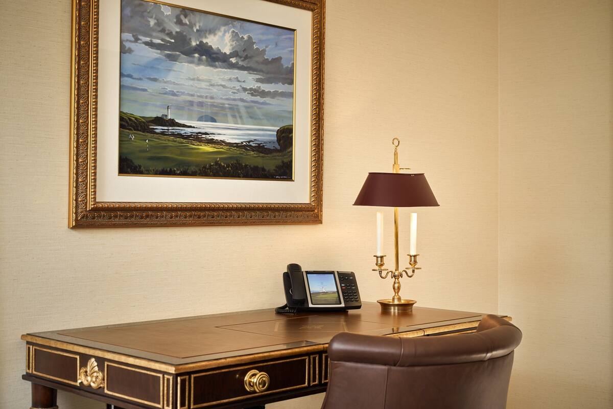 A desk with a framed landscape painting, a telephone, and a desk lamp.