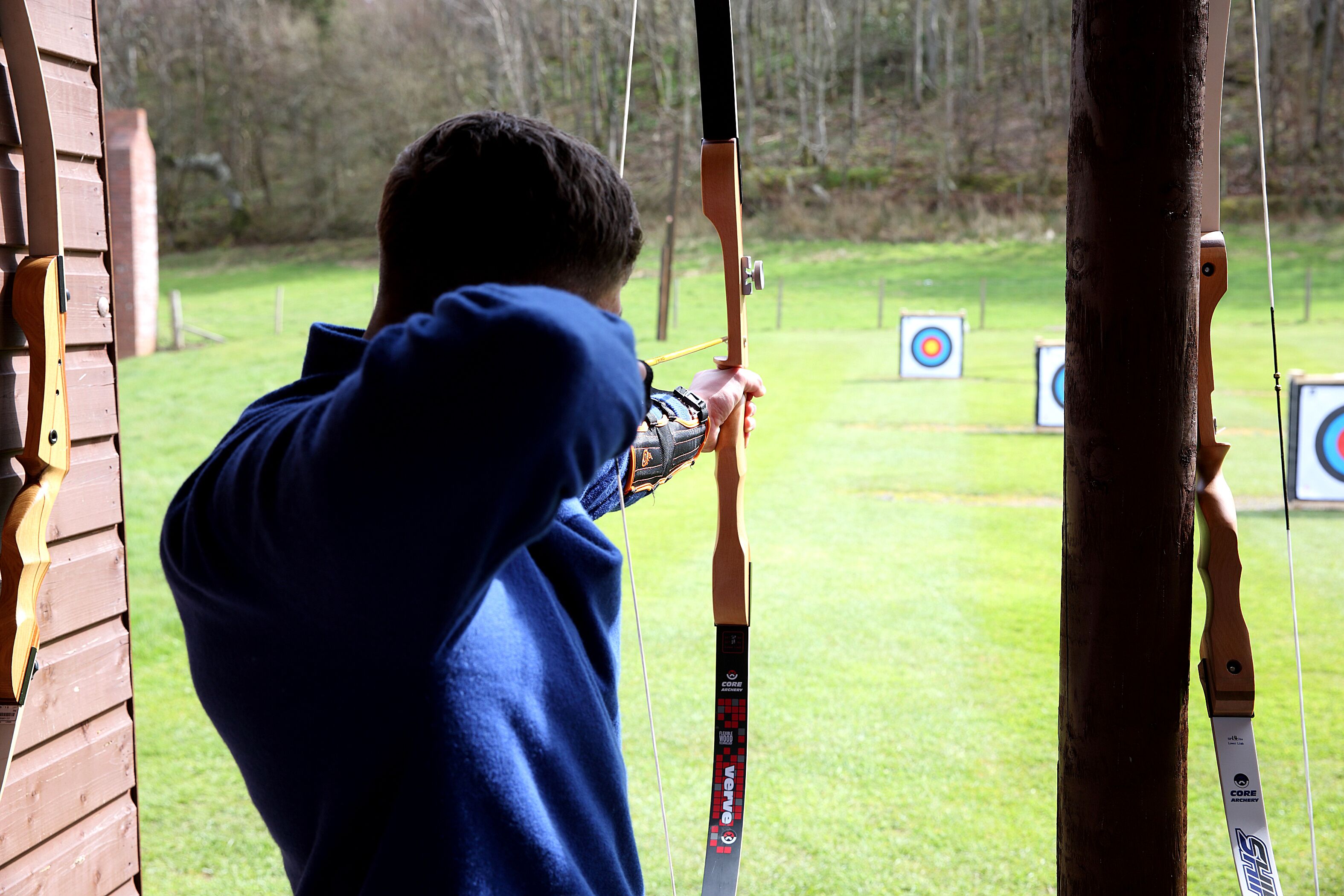 A person aiming a bow at targets in an outdoor setting.