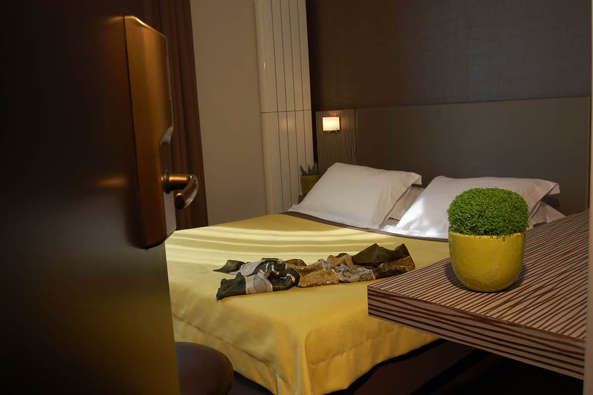 A hotel room with a bed, a bedside table, a potted plant, and a nightstand.
