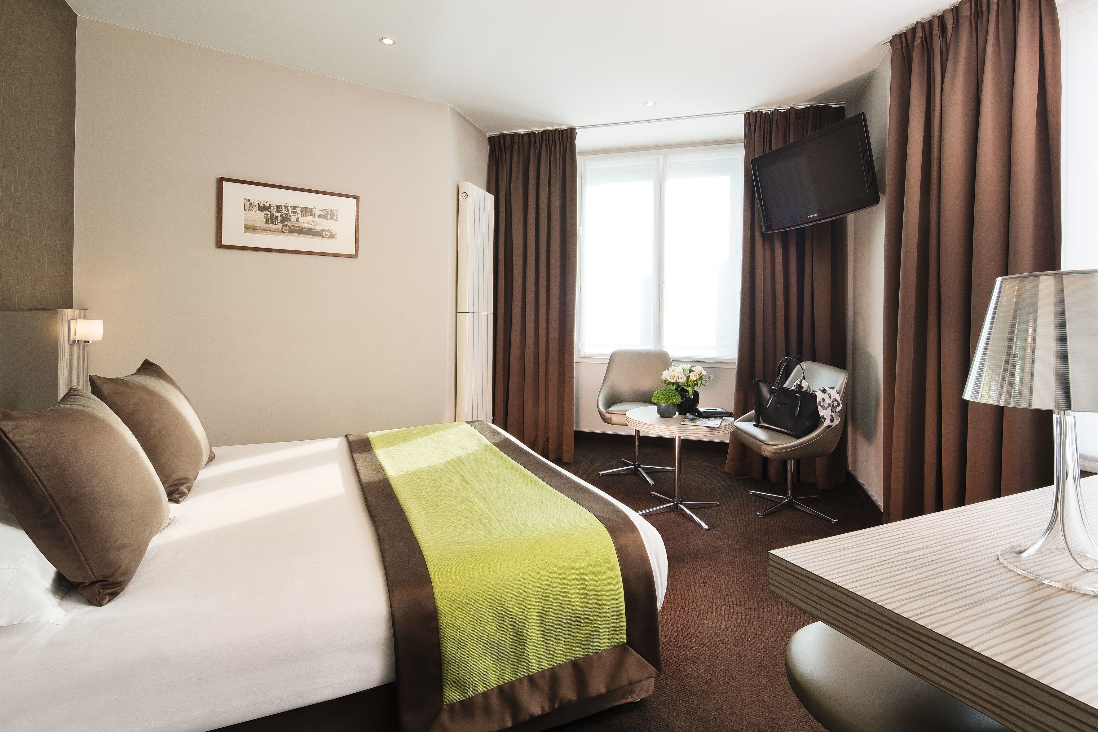 Habitación de hotel con cama, escritorio, silla, televisor y un cuadro en la pared.