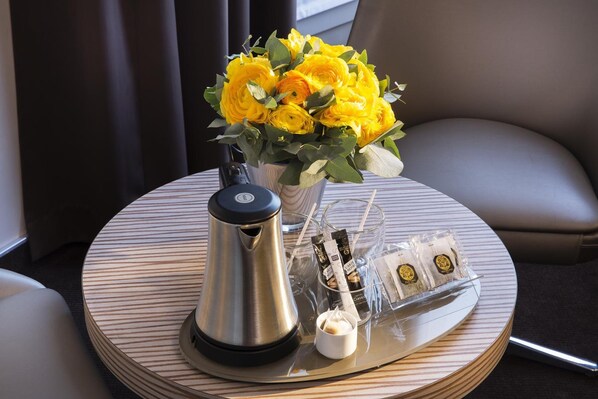 Une table ronde avec une machine à café, un vase de fleurs jaunes et un plateau contenant des sachets de café et une petite tasse de crème.
