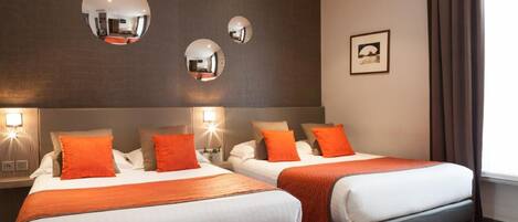 Habitación de hotel con dos camas, cada una con cabecera, y un espejo grande en la pared. Se observa un cuadro enmarcado en la pared y una ventana con cortinas.