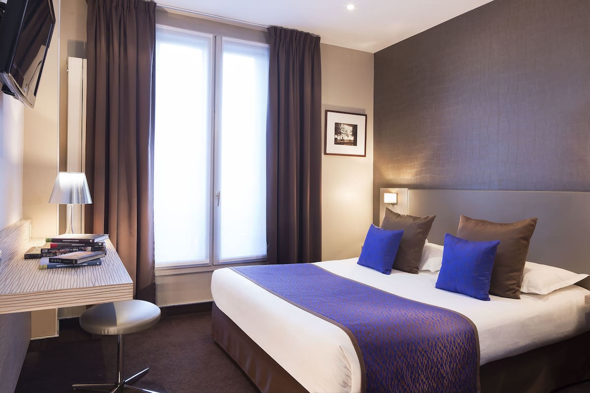 A hotel room with a bed, a desk, and a chair.