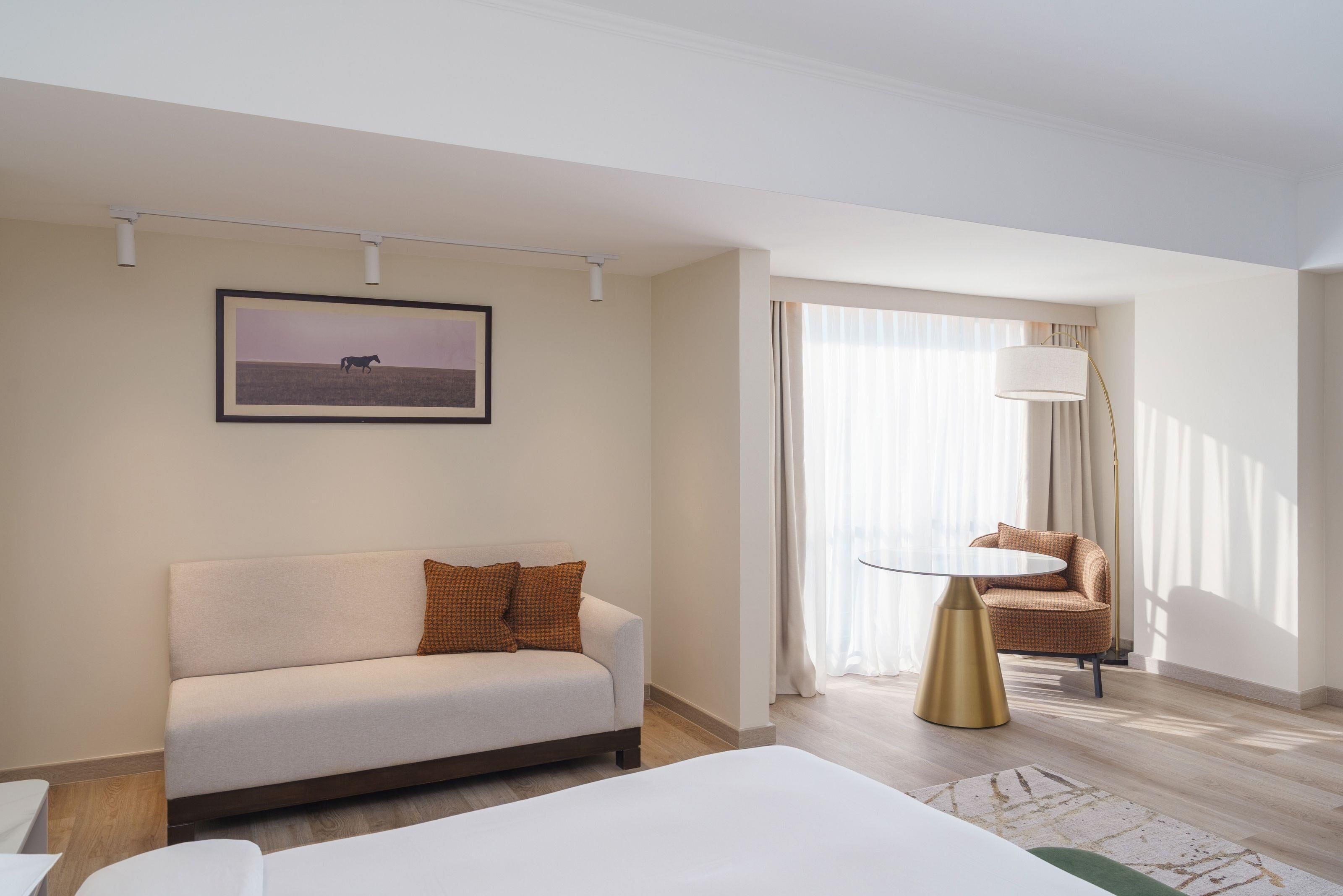 A hotel room with a sofa, a chair, a bed, a lamp, and a window with curtains.