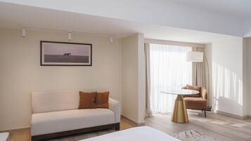 A hotel room with a sofa, a chair, a bed, a lamp, and a window with curtains.