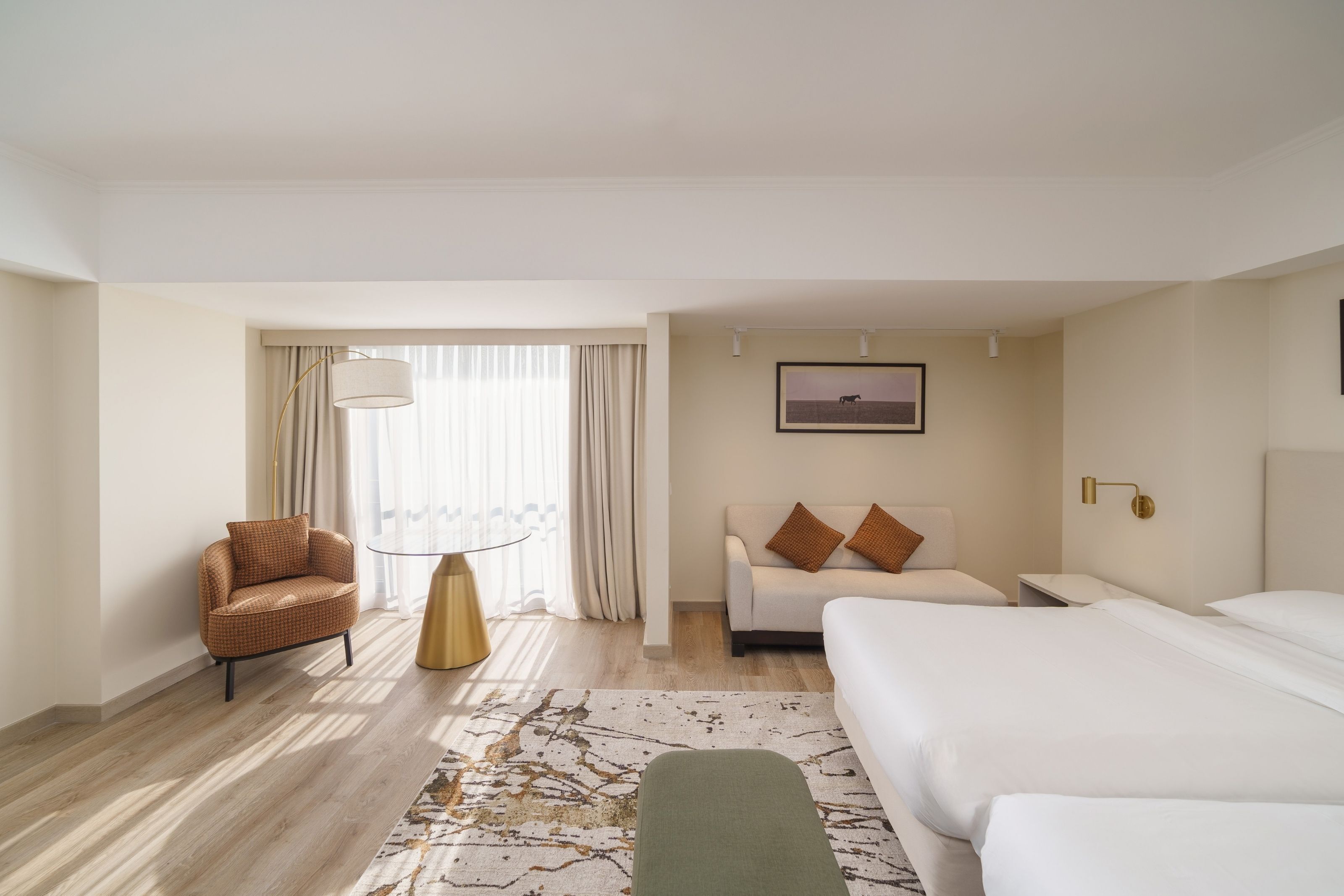 A hotel room with a bed, a sofa, a chair, a lamp, and a window with curtains.