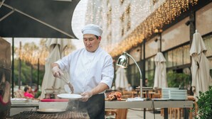 A chef cooking outdoors with a grill, tables, and umbrellas. - Hyatt Regency Bishkek (Bishkek)