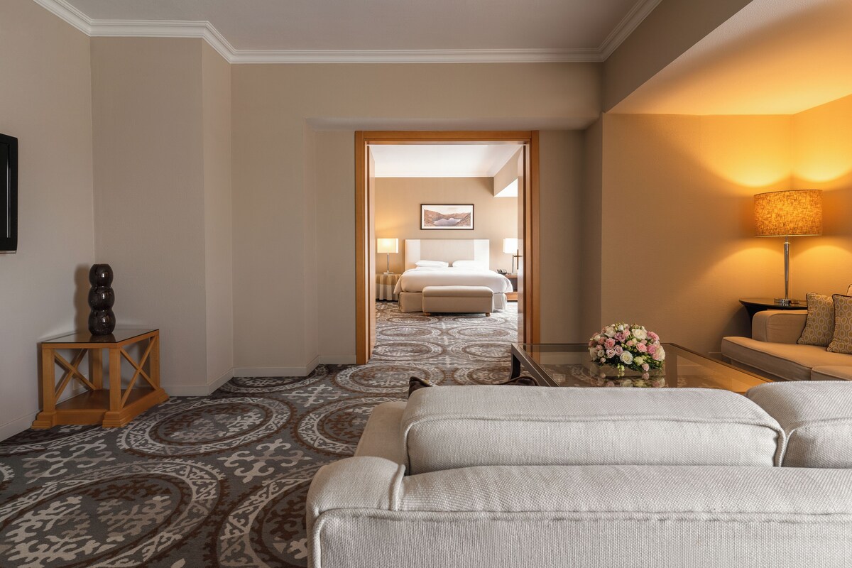 A hotel room with a large bed, a sitting area with a sofa, a small table, and a lamp.