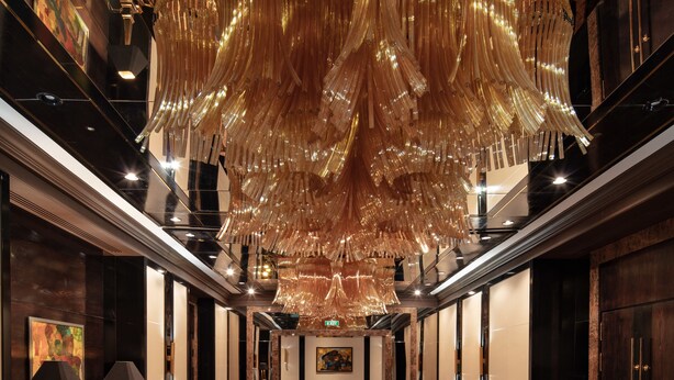 A luxurious hotel corridor with a grand chandelier, elegant wooden paneling, and a patterned carpet. - Hyatt Regency Bishkek (Bishkek)