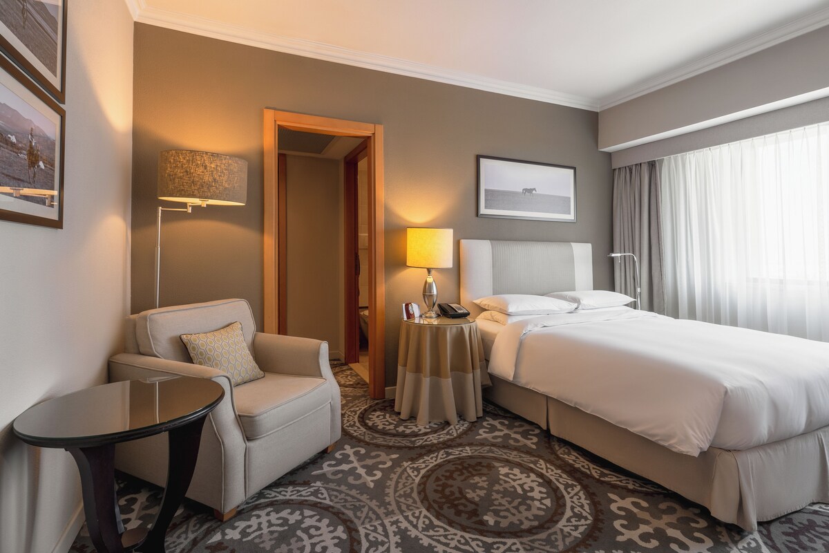 A hotel room with a bed, a sofa, a small table with a lamp, and a patterned carpet.