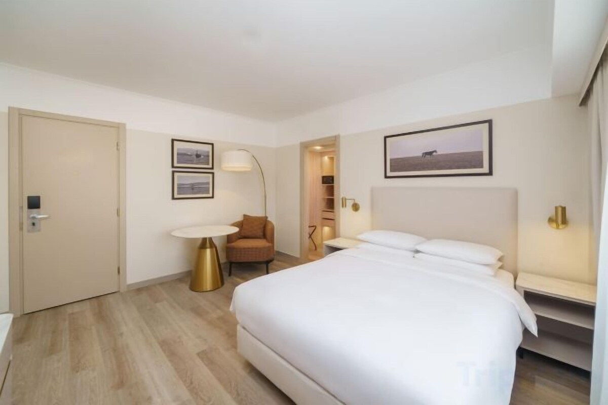 A hotel room with a bed, a chair, a desk, and a door.