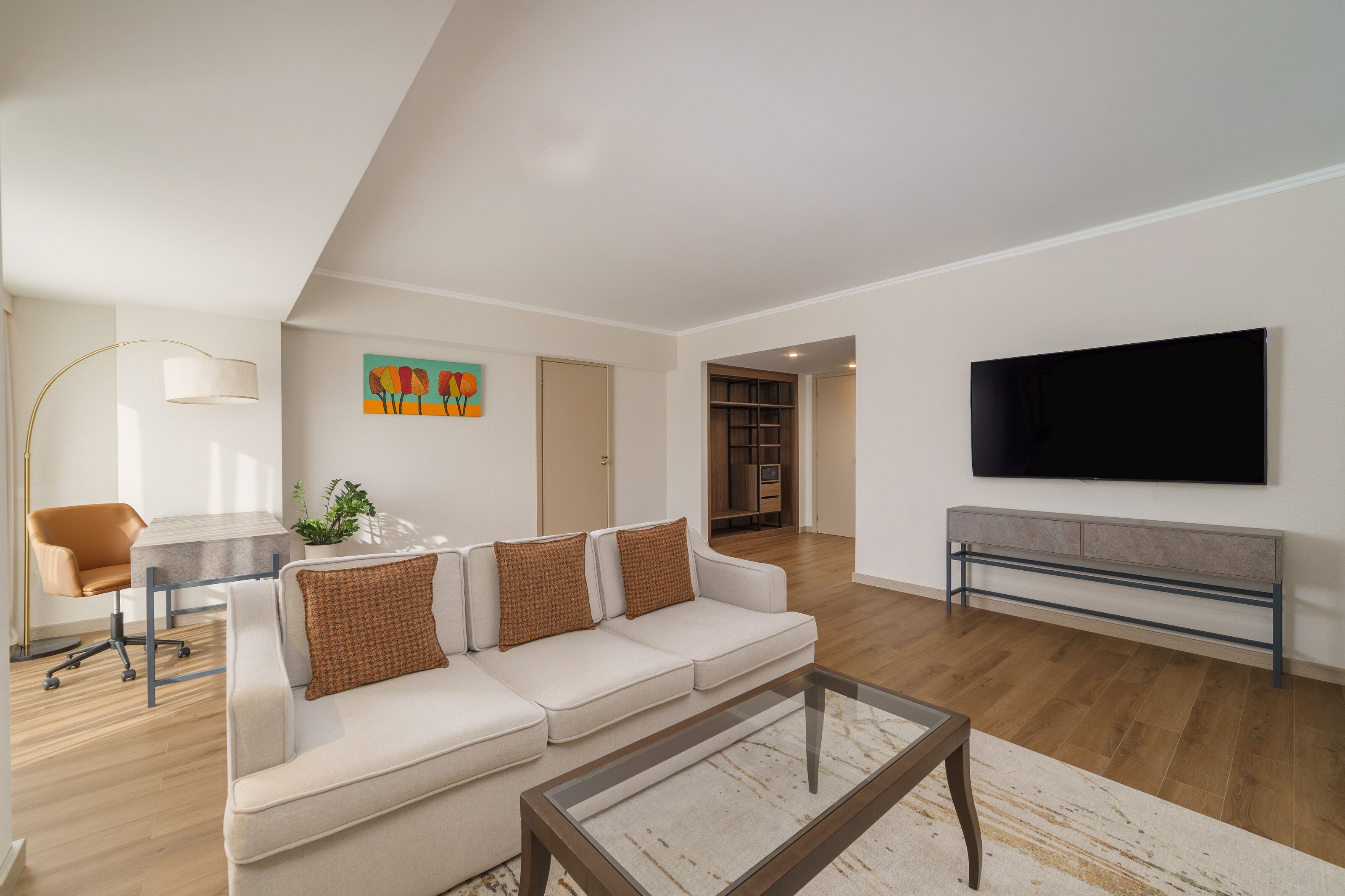 A modern living room with a sofa, coffee table, TV, and a desk with a chair.