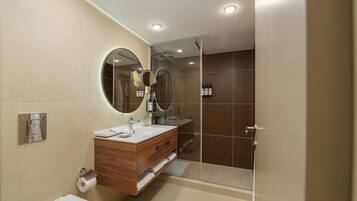 Un baño moderno con tocador de madera, espejo redondo, cabina de ducha de vidrio y retrete.