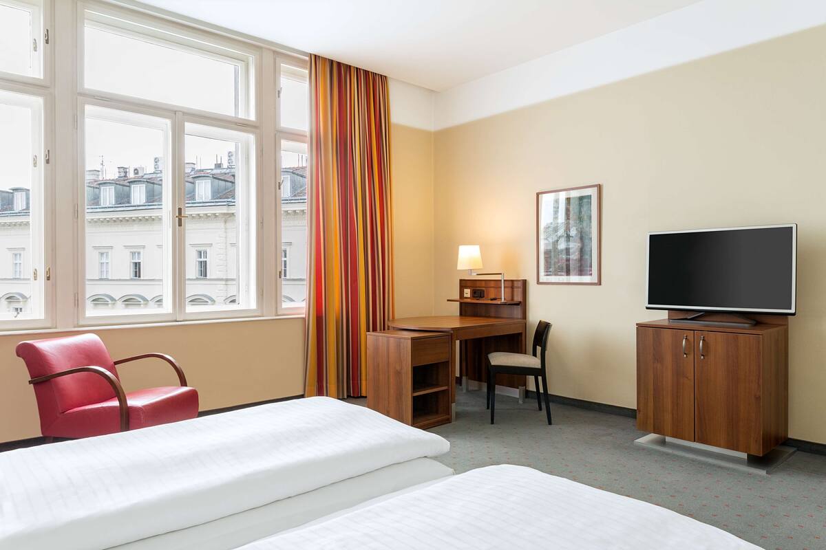 A hotel room with two beds, a desk, a chair, a television, and a window with curtains.