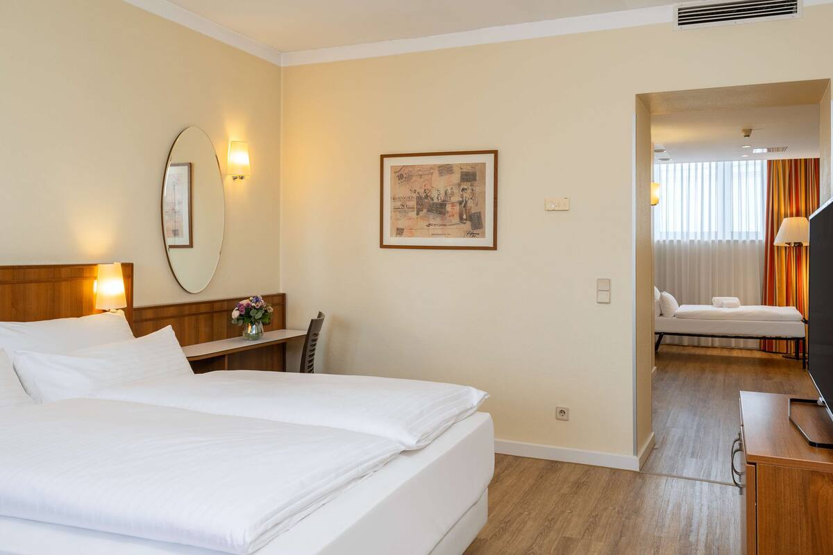A hotel room with two beds, a desk, a chair, a mirror, a framed picture, and a television.