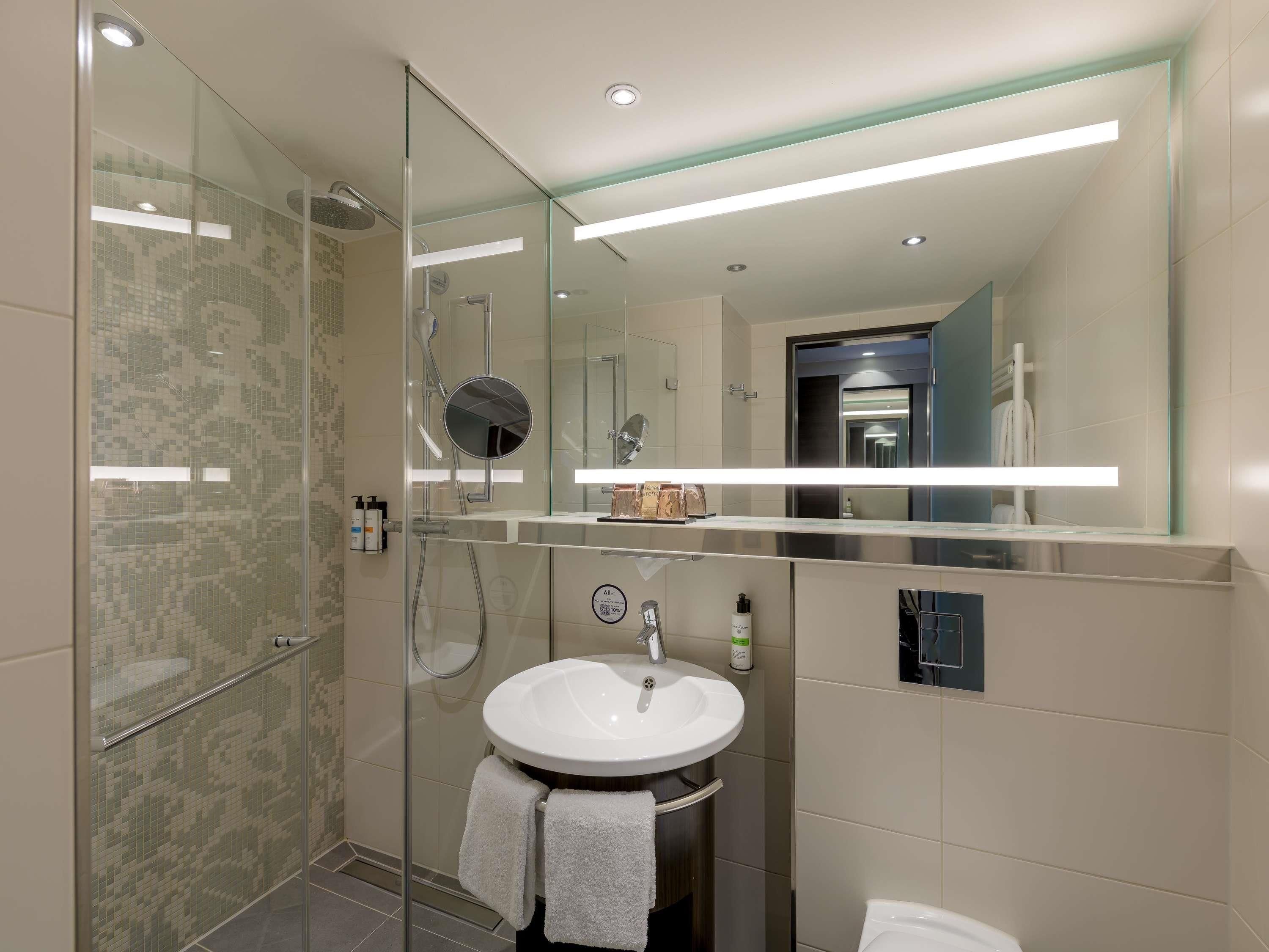 A modern bathroom with a glass shower enclosure, a white sink with a mirror above it, and a towel rack with towels.