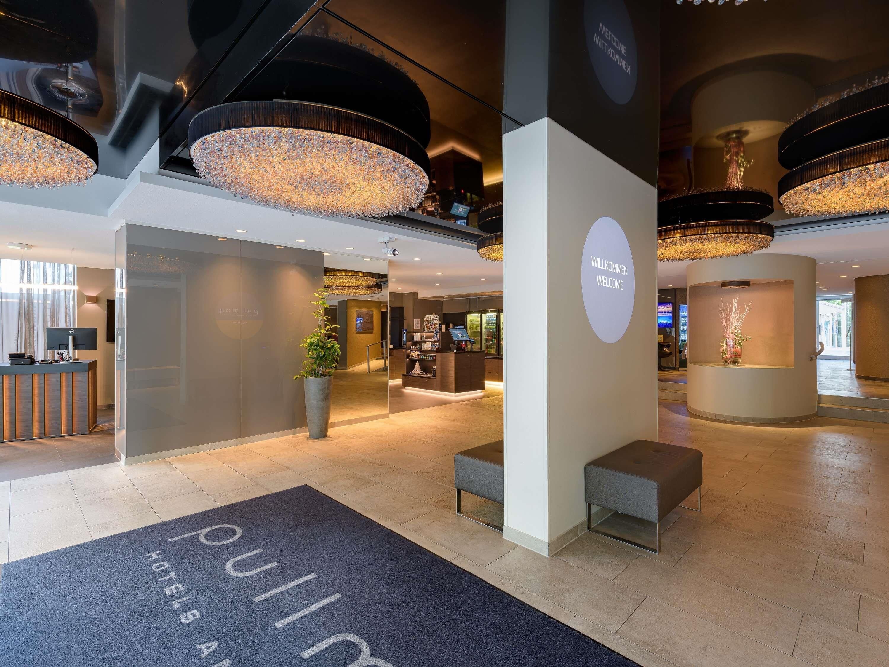 A hotel lobby with a reception desk, seating areas, and a large chandelier.