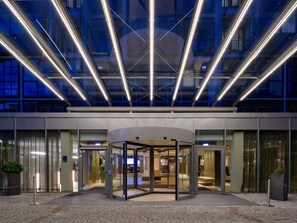 Ein moderner Hotelzugang mit einer Doppeltür, Glastüren und einem gepflasterten Bereich mit Blumentöpfen.