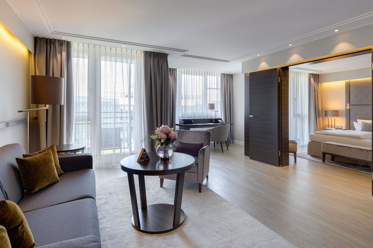 Una habitación de hotel moderna con sofá, una mesa redonda con un jarrón, cama y zona de escritorio.