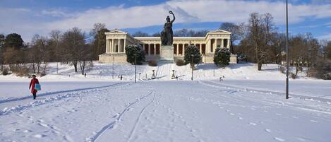 Un parque cubierto de nieve con una estatua y arquitectura clásica.
