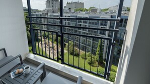 A balcony with a table, a cup, and pastries. It overlooks a courtyard with greenery and buildings in the background. - Pullman Munich (Munich)