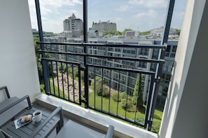 Un balcon avec une table, une tasse et des pâtisseries. Il donne sur une cour intérieure agrémentée de verdure, avec des bâtiments en arrière-plan.