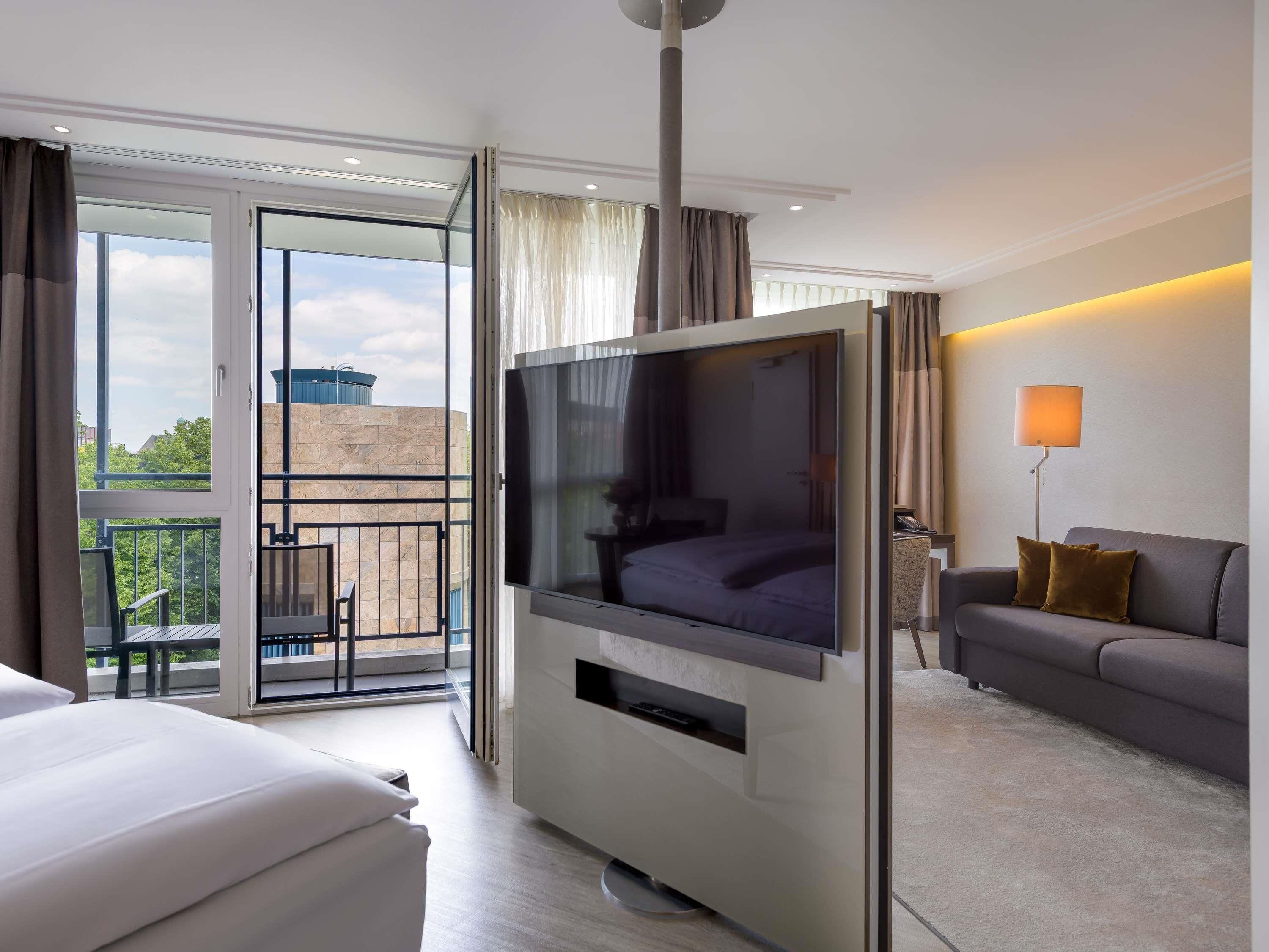 Une chambre d’hôtel avec un lit, un canapé, une télévision, un balcon avec vue et une lampe.