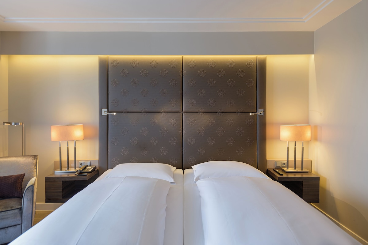 A hotel room with a large bed, two bedside tables, a chair, and a lamp.