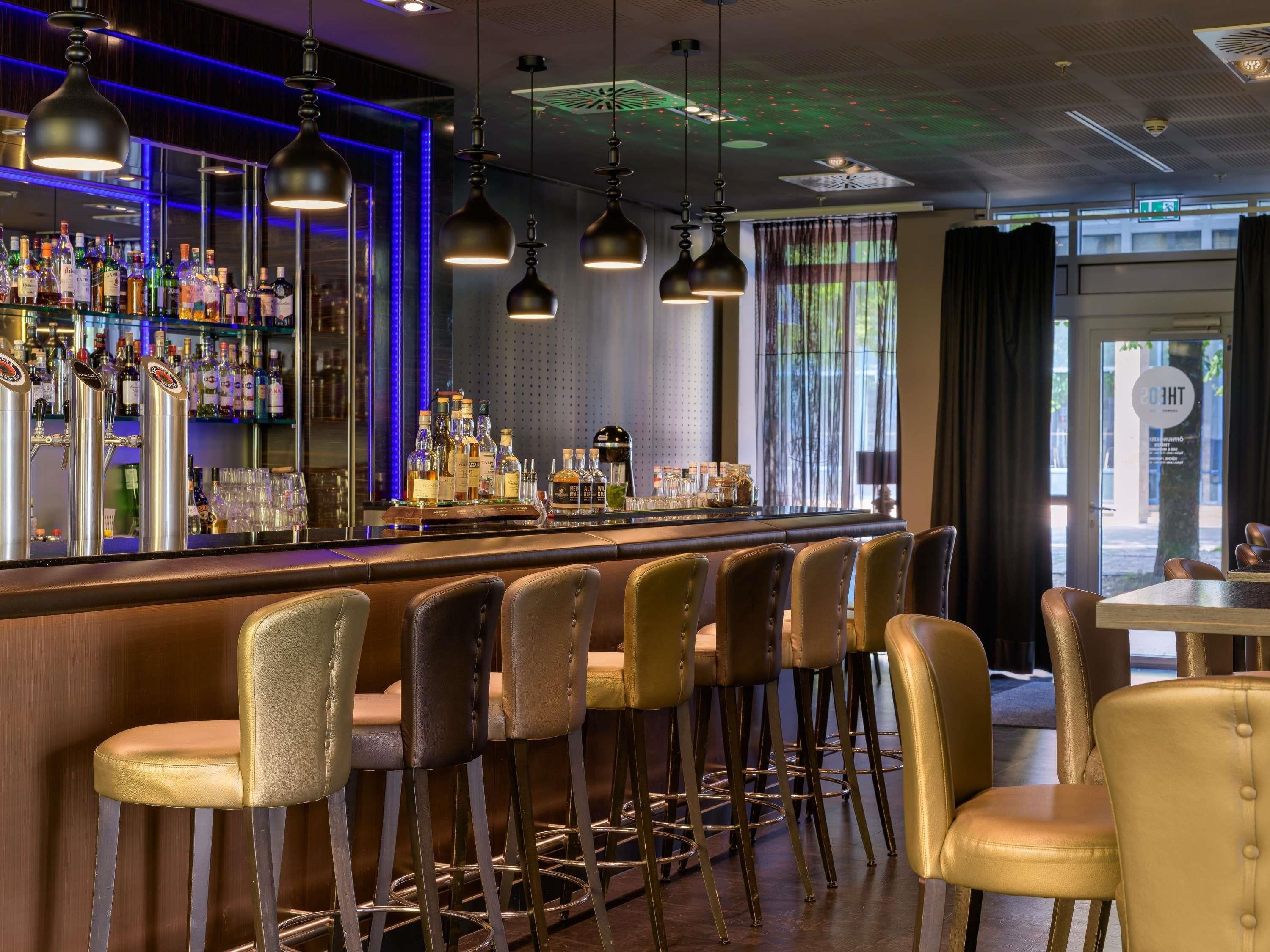 A bar area with multiple stools, a bar counter stocked with bottles, and hanging pendant lights.