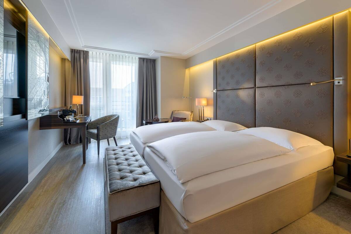 Habitación de hotel con una cama grande, un escritorio, una silla y un banco.