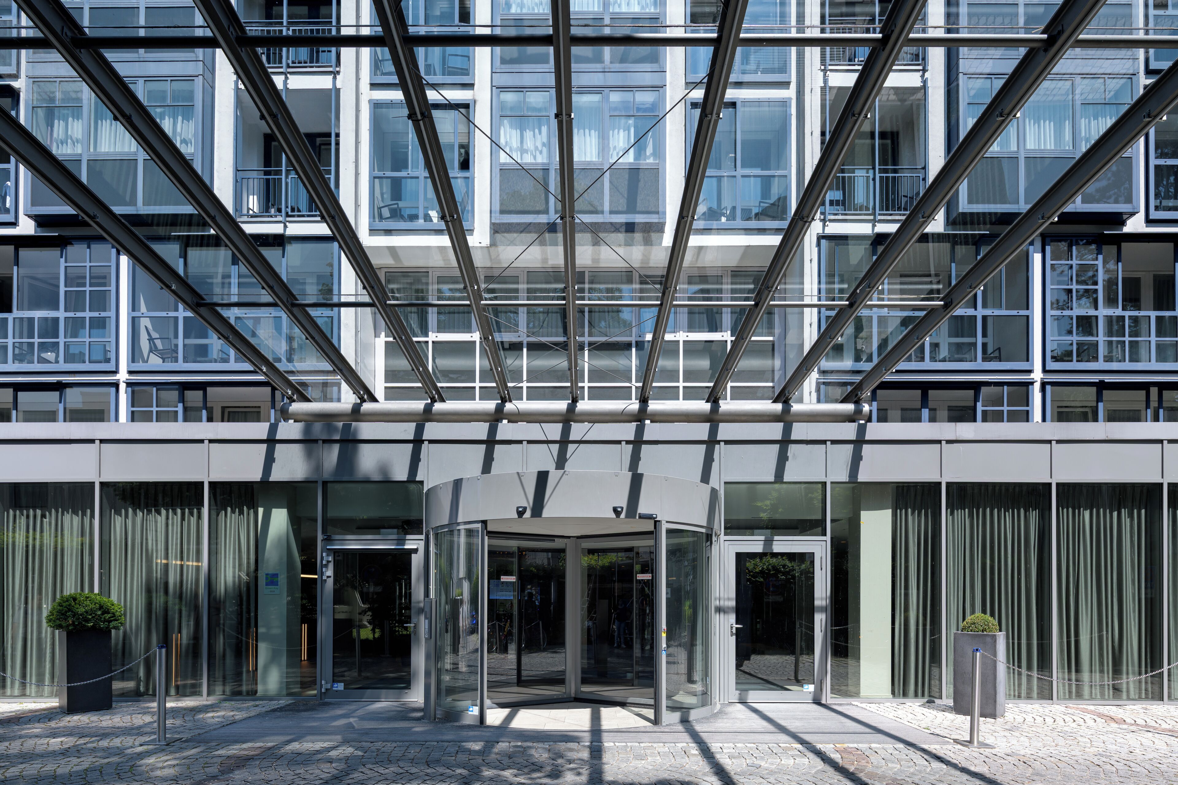 A modern building with a glass entrance, metal framework, and a potted plant.