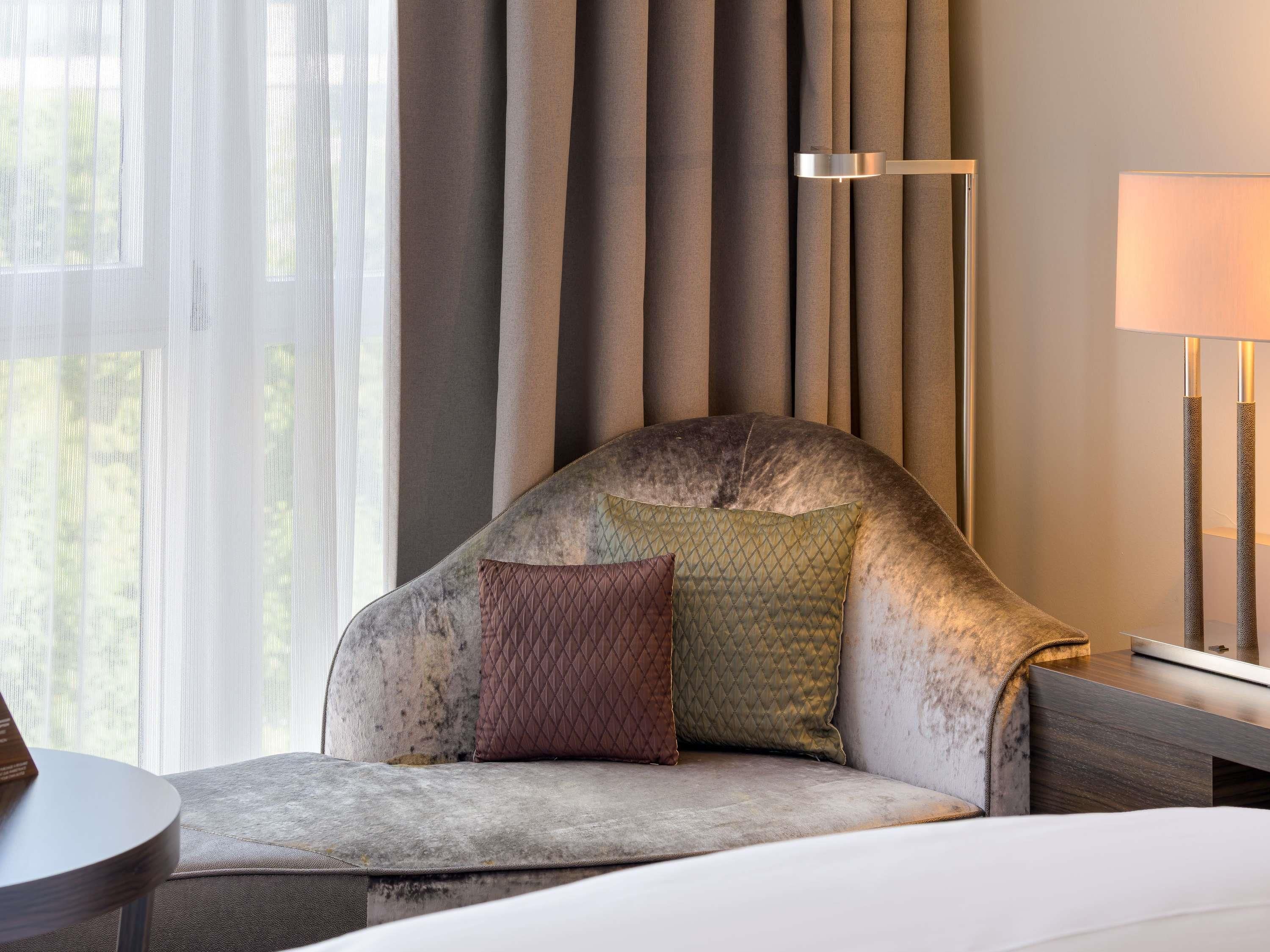 A modern hotel room with a curved sofa, a bedside table, and a lamp.