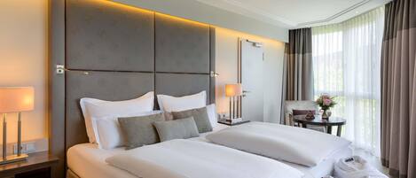 A hotel room with a large bed, bedside tables, a small table with a vase, and a view of the outdoors.