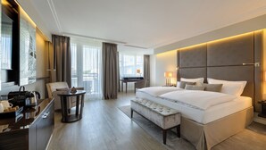A modern hotel room with a large bed, a desk, a chair, and a view of the outdoors. - Pullman Munich (Munich)