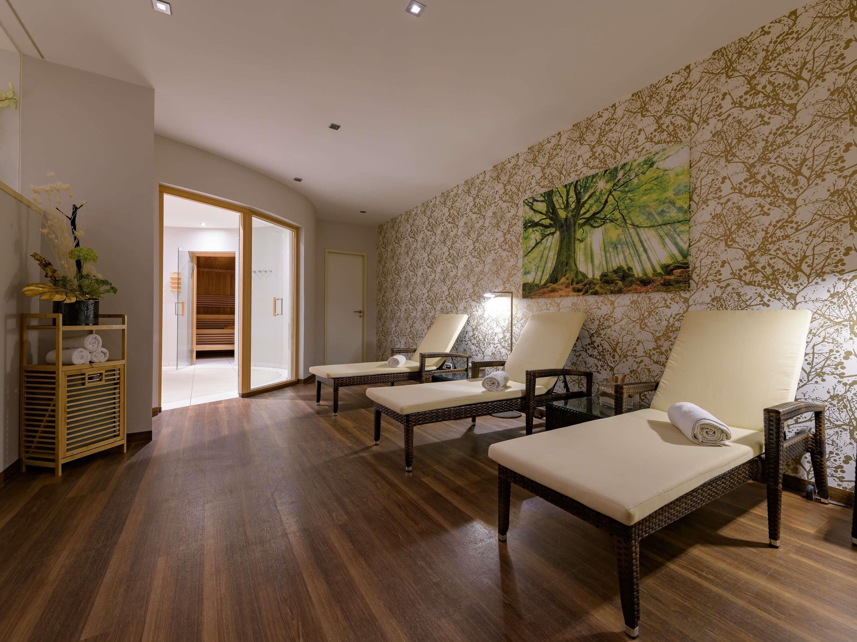 Un cuarto de spa con dos sillas de masaje, piso de madera, ducha de vidrio y un árbol pintado en la pared.
