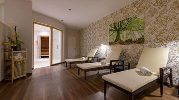 Un cuarto de spa con dos sillas de masaje, piso de madera, ducha de vidrio y un árbol pintado en la pared.