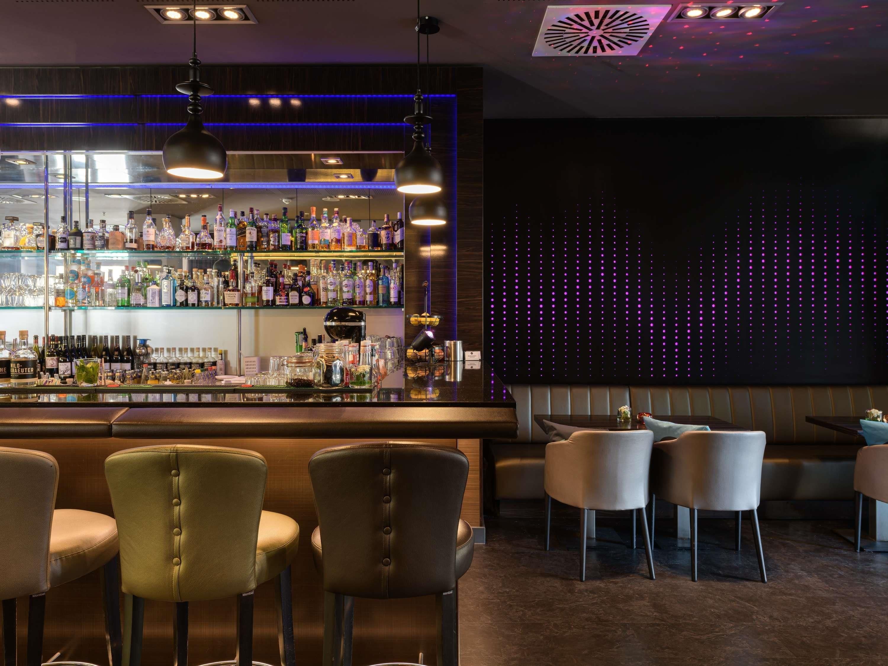A bar area with multiple shelves of liquor bottles, a bar counter, and several chairs.