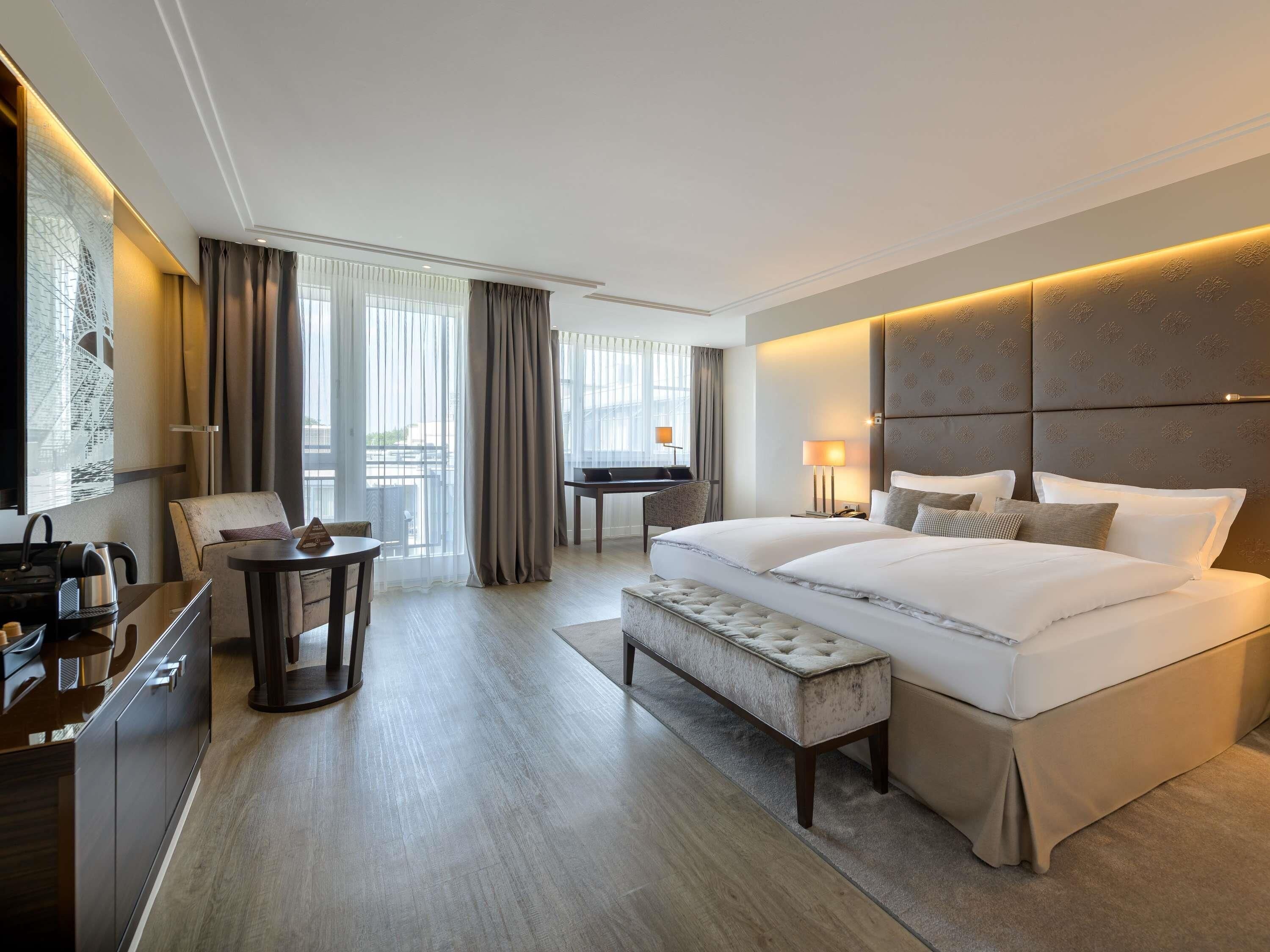 Ein modernes Hotelzimmer mit einem großen Bett, einem Schreibtisch, einem Stuhl und Blick ins Freie.